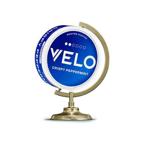 Velo Nicotine Pouches |  A blue VELO Crispy Peppermint nicotine pouch container is displayed on a small, gold globe stand against a white background, showcasing the sleek design of VELO pouches.