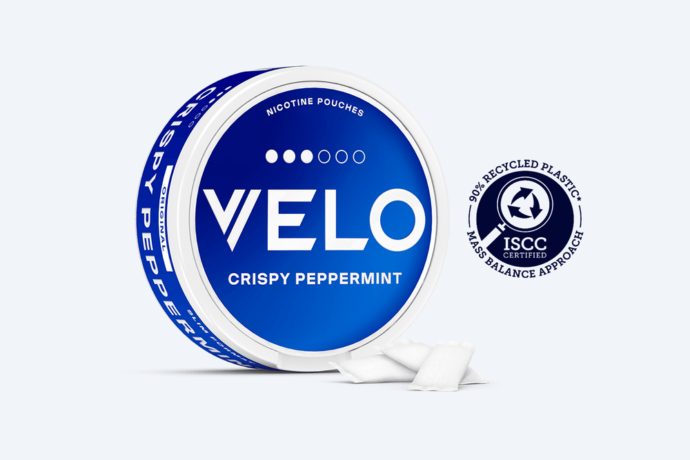 Velo Nicotine Pouches |  Round blue VELO CRISPY PEPPERMINT nicotine pouches container with three VELO pouches beside it. Badge reads ISCC Certified and 30% Recycled Plastic. White background.