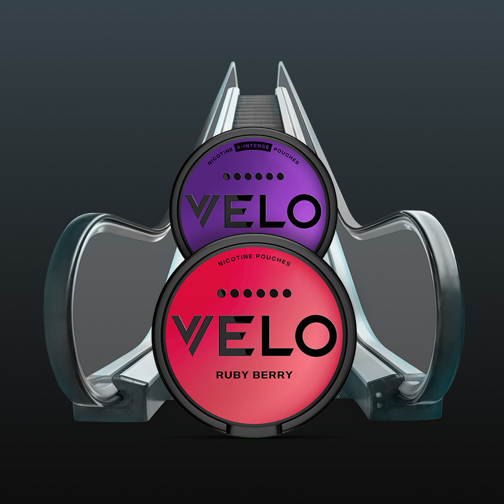 Velo Nicotine Pouches |  Two round VELO nicotine pouch containers, one purple and one pink, are placed in front of an escalator on a dark background. The sleek pouches highlight Velo’s modern approach to nicotine enjoyment.