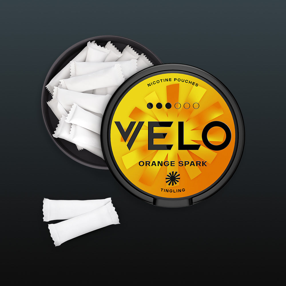 Velo Nicotine Pouches |  A round container of VELO Orange Spark nicotine pouches, partly open to show white pouches inside. Three additional nicotine pouches are placed next to the container on a dark background.