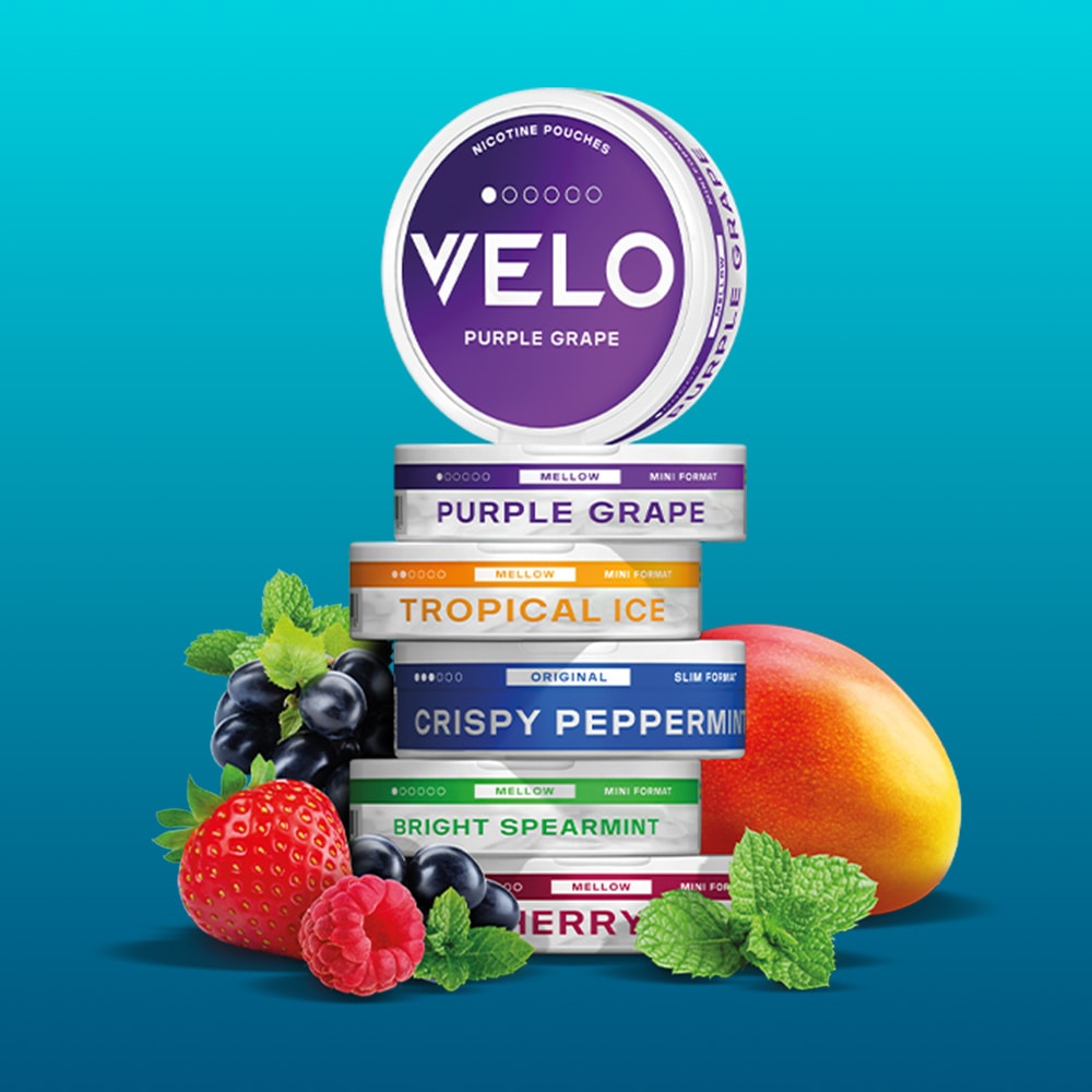 Velo Nicotine Pouches |  A stack of Velo nicotine pouches in various flavors, such as strawberry, blackcurrant, mint, and mango, is arranged with fruit and mint leaves on a turquoise background.