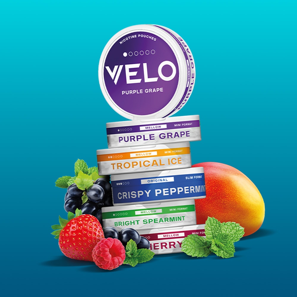 Velo Nicotine Pouches |  A stack of VELO nicotine pouch containers in various flavors with fresh fruits and mint leaves, set against a blue background, highlights the refreshing appeal of these innovative nicotine pouches.