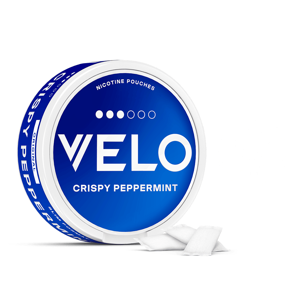 Velo Nicotine Pouches |  A round blue and white tin labeled VELO Crispy Peppermint Nicotine Pouches sits on a plain white background, with a few of the refreshing Velo nicotine pouches placed neatly beside it.