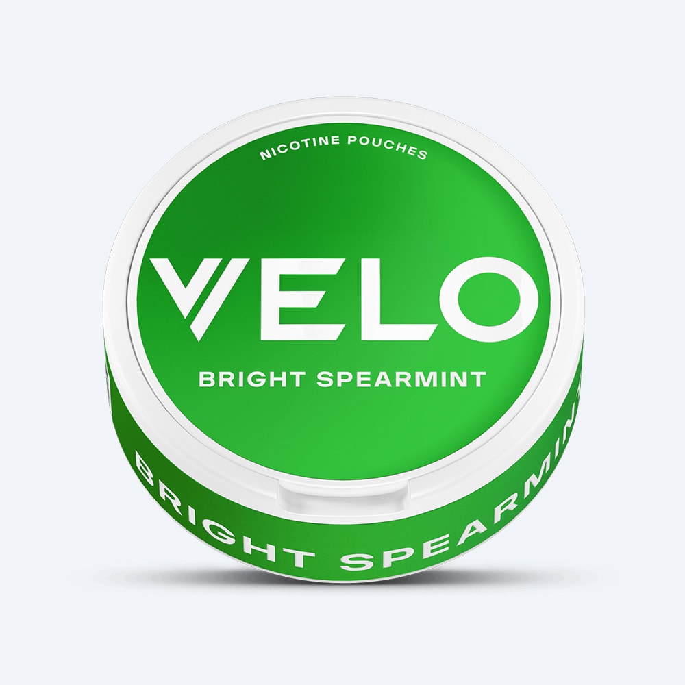 Velo Nicotine Pouches |  A round white container with a green lid, labeled VELO Bright Spearmint, features text above that reads "Nicotine Pouches" and emphasizes a refreshing spearmint and cool menthol flavor experience.