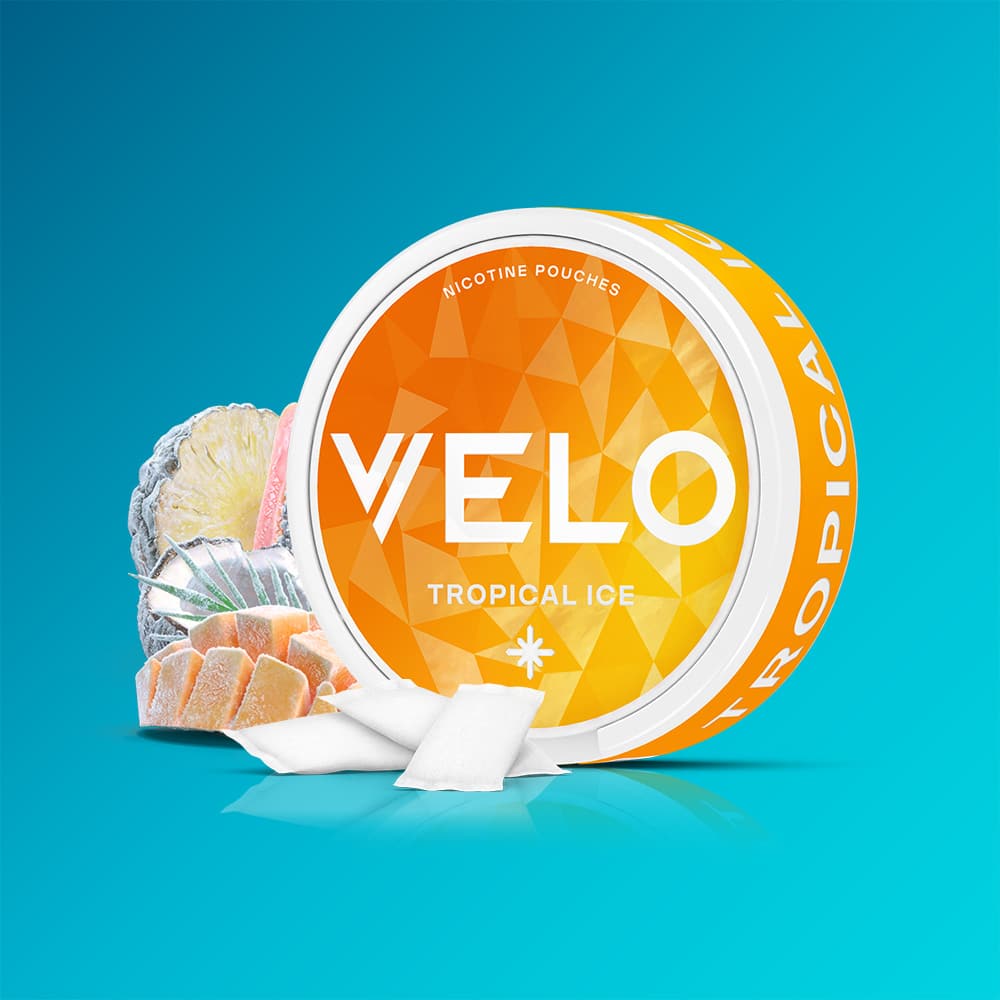 Velo Nicotine Pouches |  A VELO Tropical Ice nicotine pouch container in a round, bright orange design is displayed with white pouches and slices of tropical fruit in front, set against a gradient blue background to emphasize the vibrant Tropical Ice flavour and its refreshing cooling sensation.