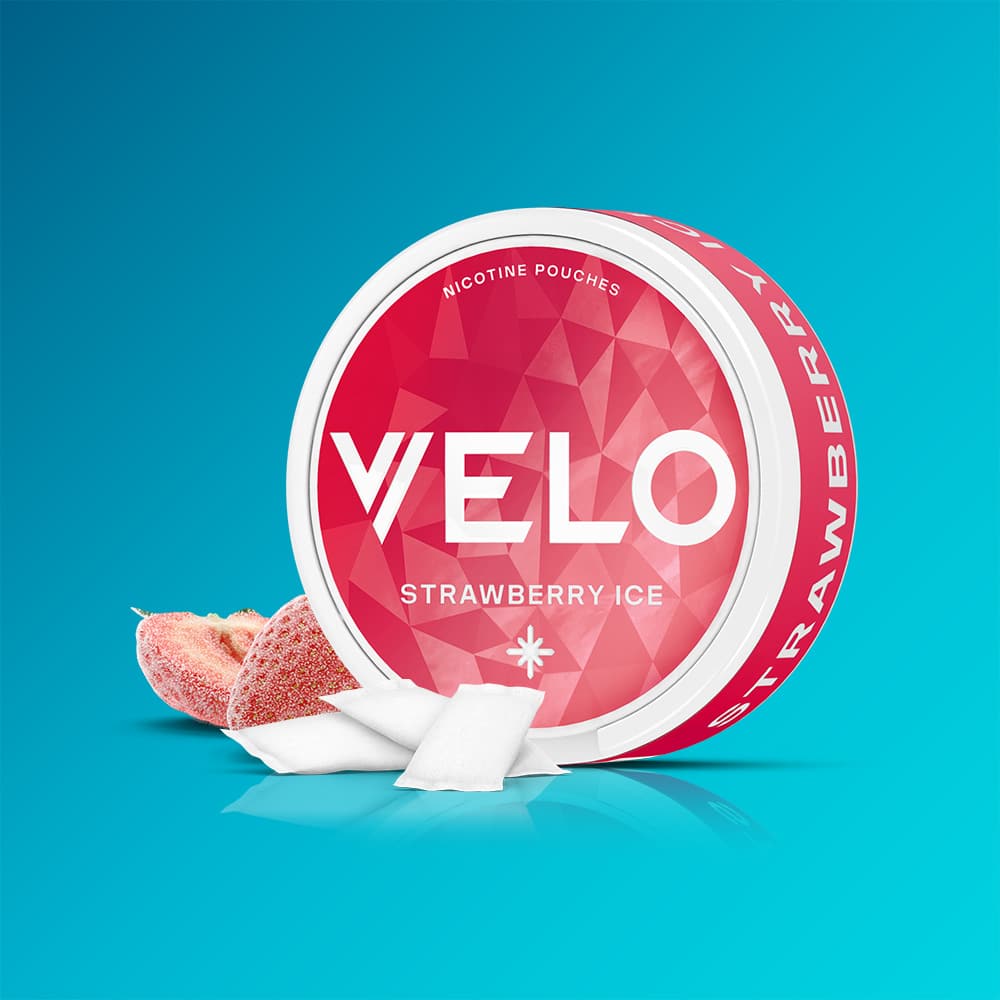 Velo Nicotine Pouches |  A round container of VELO Strawberry Ice sits on a blue background, accompanied by several nicotine pouches and a sliced strawberry beside the container.