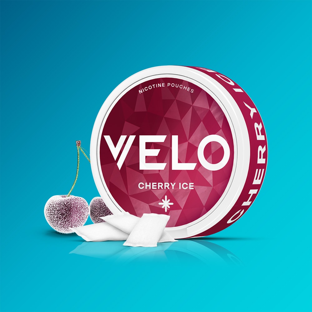 Velo Nicotine Pouches |  A round tin of VELO Cherry Ice sits on a vibrant blue background. The tin displays a deep red, geometric design that suggests the fruity flavour inside. Beside it lie three white NICOTINE POUCHES and a pair of cherries with a frosty, textured look—capturing the refreshing cooling sensation of Cherry Ice.