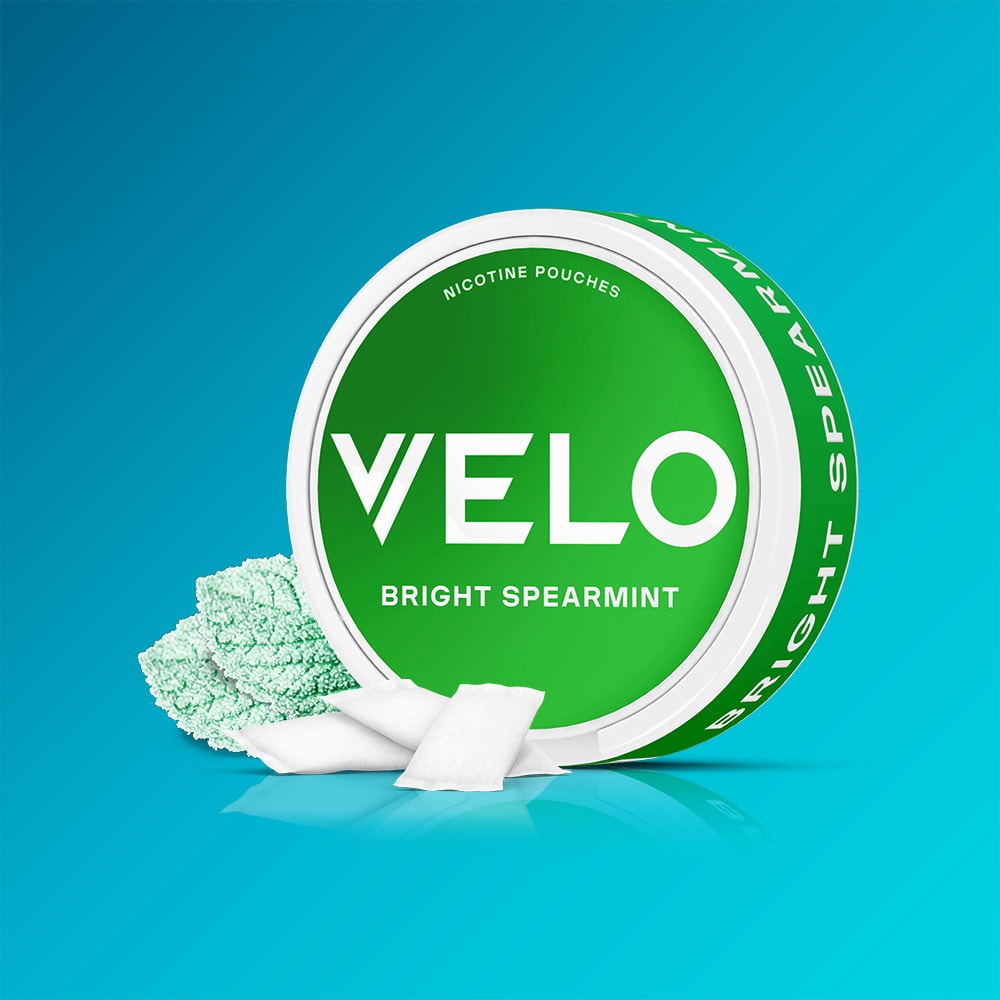 Velo Nicotine Pouches |  A green can labeled VELO Bright Spearmint features white nicotine pouches and fresh spearmint leaves, evoking a crisp menthol sensation against a blue gradient background.