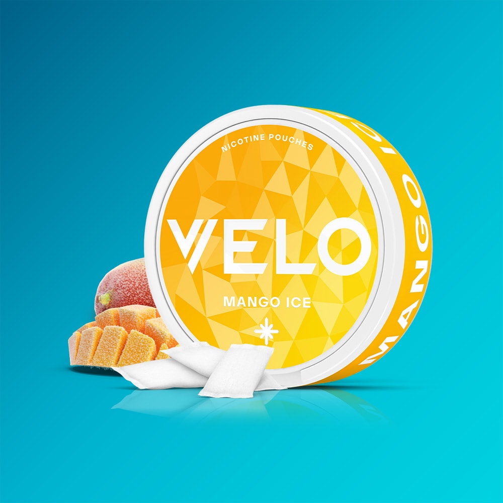 Velo Nicotine Pouches |  A round container of VELO Mango Ice sits next to juicy mango cubes and a fresh mango slice on a blue gradient background, evoking the tangy mango taste and cool sensation of its nicotine pouches. Two white pouches are placed in front of the container.
