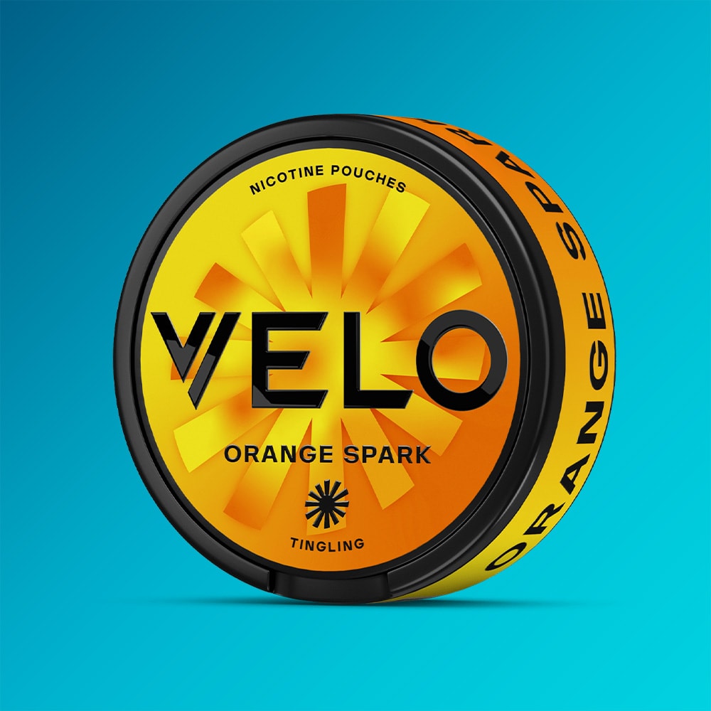 Velo Nicotine Pouches |  A round container of VELO Orange Spark nicotine pouches, featuring vibrant orange and yellow packaging, is set against a blue background. The label displays the words "Tingling" and "Orange Spark," suggesting an intense tingle and a citrusy flavor inspired by zesty, ripe oranges.