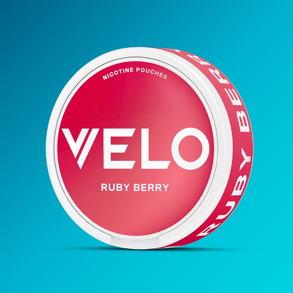 Velo Nicotine Pouches |  A VELO Ruby Berry container of nicotine pouches, featuring a lively strawberry flavor with gentle acidity, is shown against a blue gradient background. The round container displays a red and white design with prominent white text on both the lid and rim.