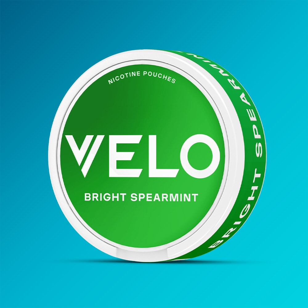 Velo Nicotine Pouches |  A round green container labeled "Bright Spearmint" by VELO stands upright on a blue gradient background, emphasizing its invigorating blend of spearmint and menthol.