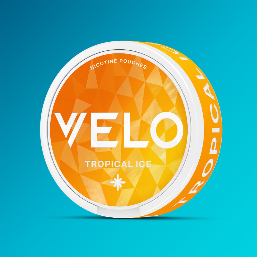 Velo Nicotine Pouches |  A round orange can of VELO Tropical Ice is displayed against a blue gradient background. The can showcases a geometric pattern, bold white branding, and suggests a vibrant fruit flavour with a refreshing cooling effect.