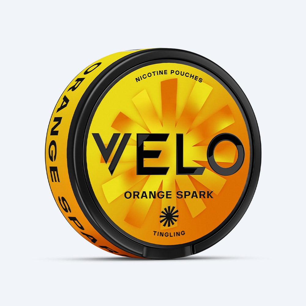 Velo Nicotine Pouches |  A round can of VELO Orange Spark nicotine pouches featuring a vibrant orange-and-yellow sunburst design with bold black lettering, offering a citrus-flavored experience inspired by zesty ripe oranges.