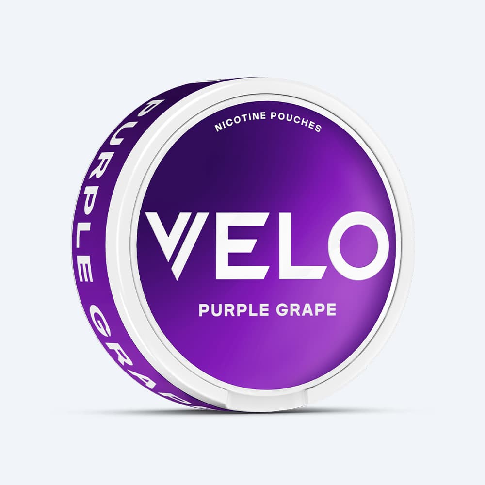 Velo Nicotine Pouches |  A round white container featuring a purple label displays the VELO brand name and reads “Purple Grape Nicotine Pouches.” The side of the container also states “Purple Grape,” emphasizing its bold flavor inspired by juicy red grapes. The background is plain white.