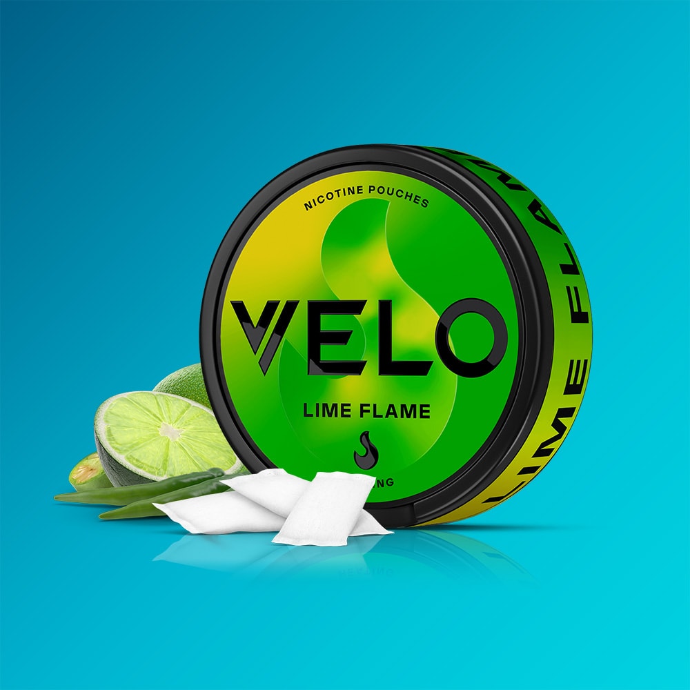 Velo Nicotine Pouches |  A round can of VELO Lime Flame nicotine pouches is shown with a sliced lime, green leaves, and three white nicotine pouches on a blue background. The packaging is green and yellow with bold black text.