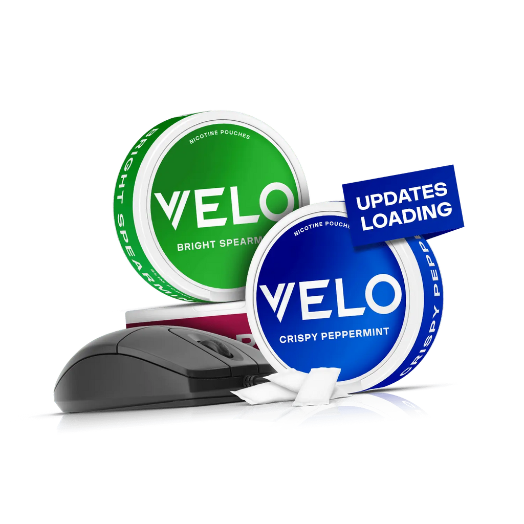 Velo Nicotine Pouches |  Two VELO nicotine pouch cans, one green (Bright Spearmint) and one blue (Crispy Peppermint), sit beside a computer mouse and paper slips. An "Updates Loading" sign appears near the blue can, highlighting the refreshingly modern appeal of Velo nicotine pouches.