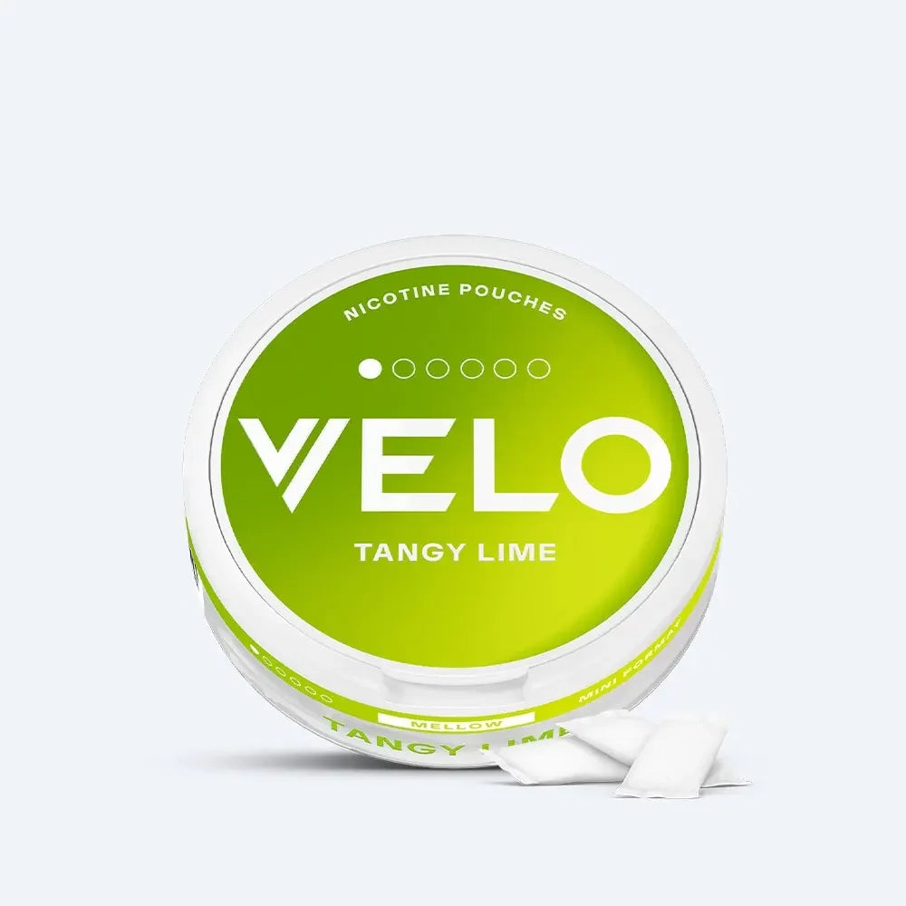 Velo Nicotine Pouches |  A round container labeled VELO Tangy Lime Nicotine Pouches with a green and white design sits on a plain light background. Two white Velo nicotine pouches are displayed in front of the container, highlighting their clean and convenient form.