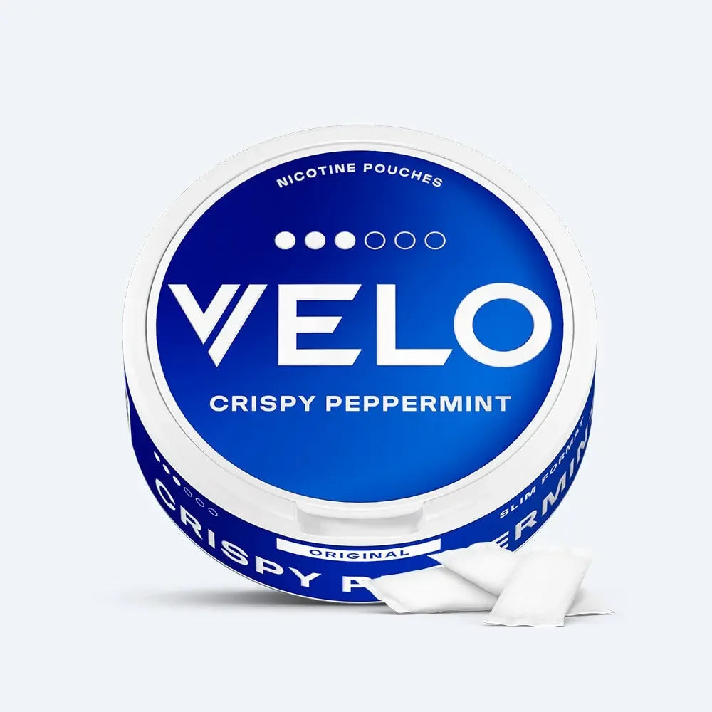 Velo Nicotine Pouches |  A round blue Velo container labeled VELO CRISPY PEPPERMINT with NICOTINE POUCHES text on top. Two white rectangular nicotine pouches are placed in front of the container.