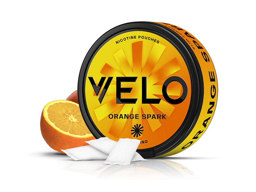 Velo Nicotine Pouches |  A round can of VELO Orange Spark nicotine pouches sits next to orange slices, with two white pouches in front. The can is yellow-orange with bold black text and a sunburst design, highlighting the vibrant flavor and refreshing nicotine experience from Velo’s signature pouches.
