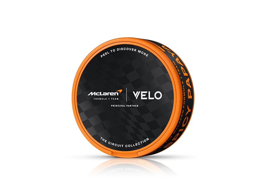 Velo Nicotine Pouches |  Round black and orange tin labeled “McLaren Formula 1 Team x VELO, Principal Partner, The Circuit Collection,” featuring a checkered pattern on the lid. This collector’s tin contains VELO nicotine pouches inspired by the high-octane world of Formula 1 racing.